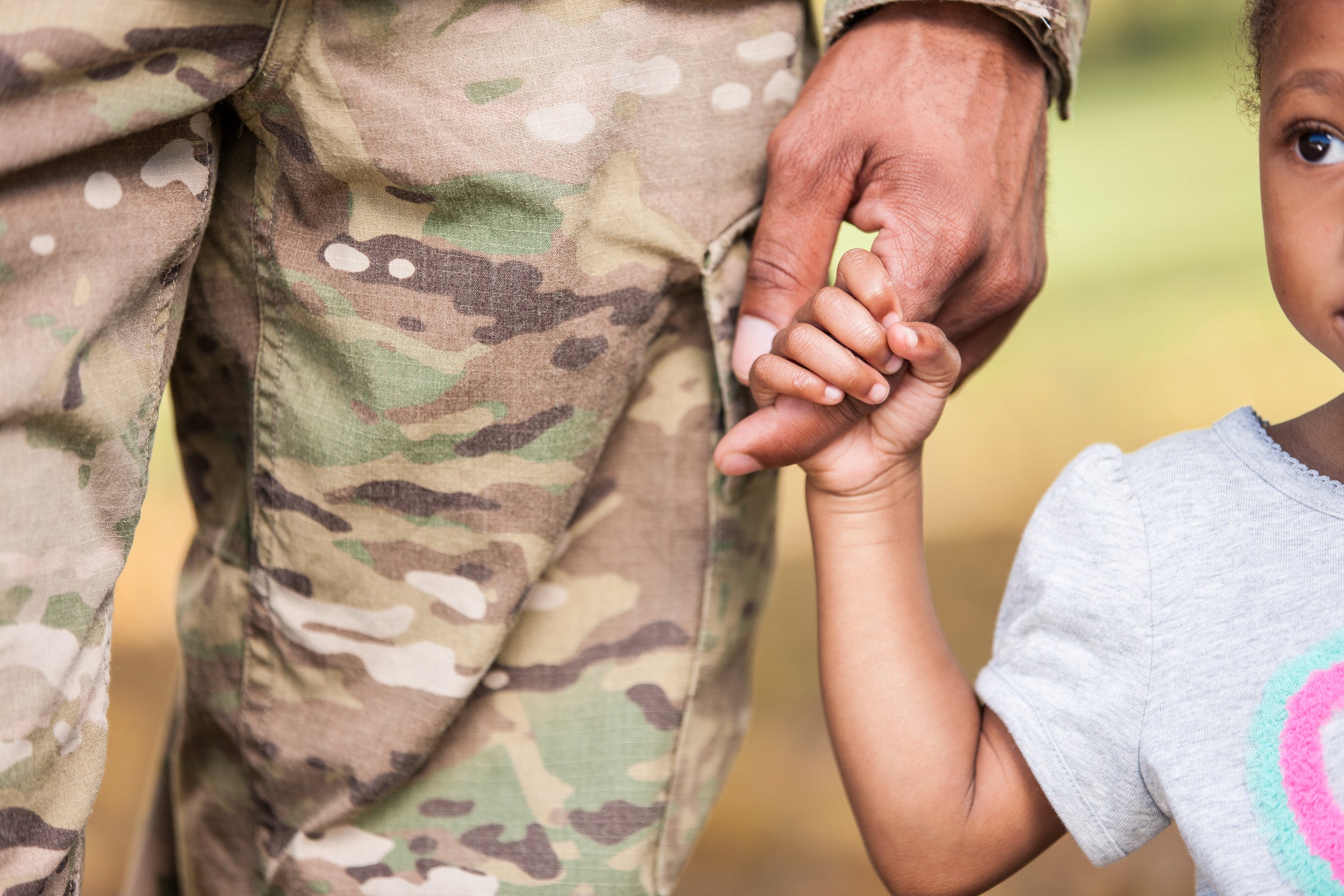 Person in camouflage holding a child's hand with a blurred background